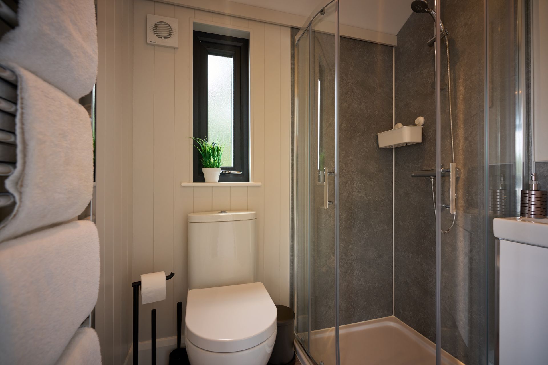 A bathroom with a toilet , sink , shower and window.