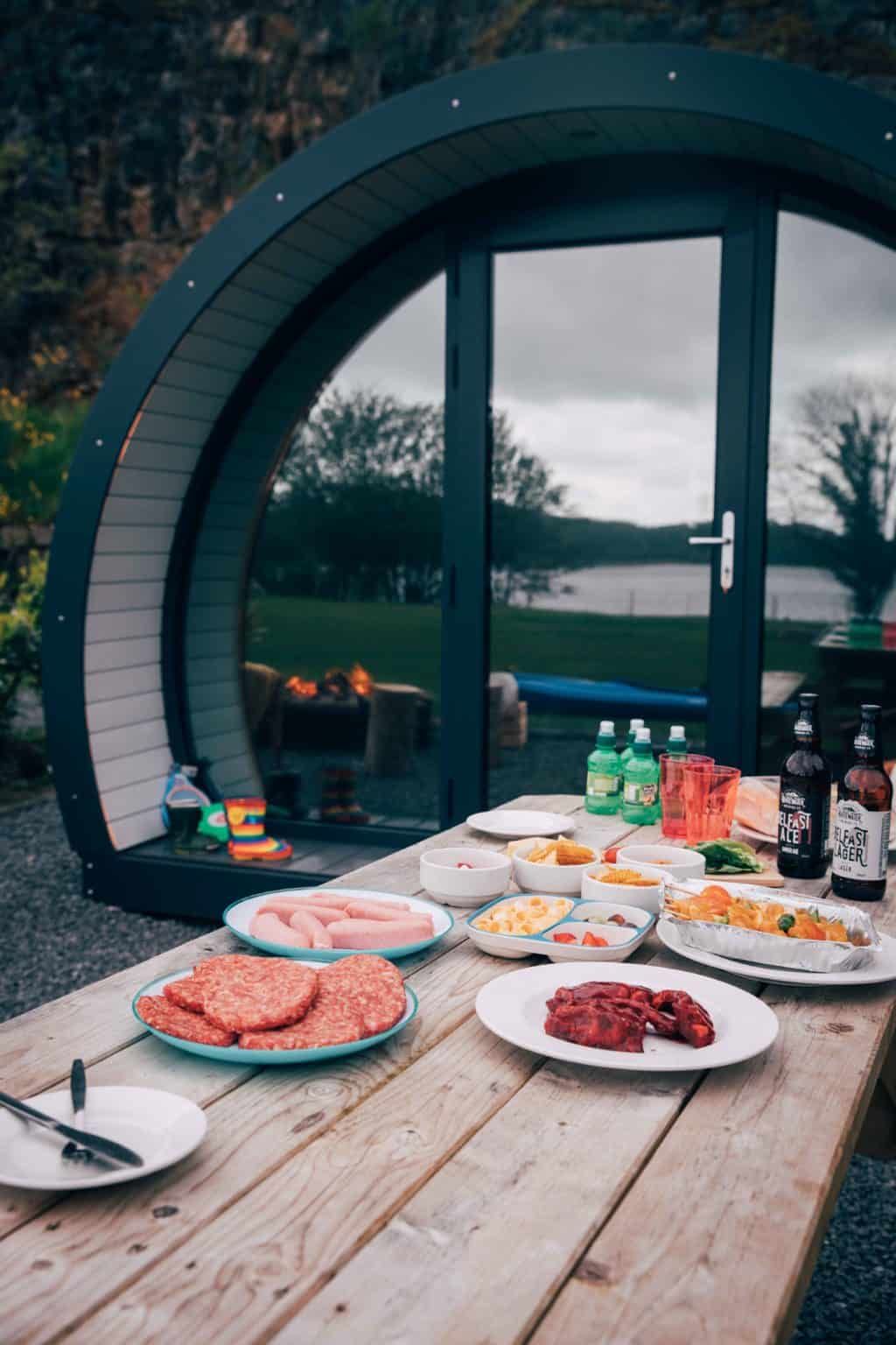 A wooden picnic table topped with plates of food and bottles of beer.