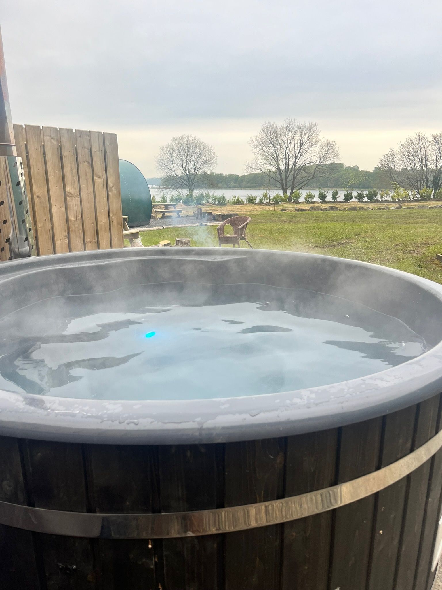 A wooden hot tub filled with water and steam coming out of it.
