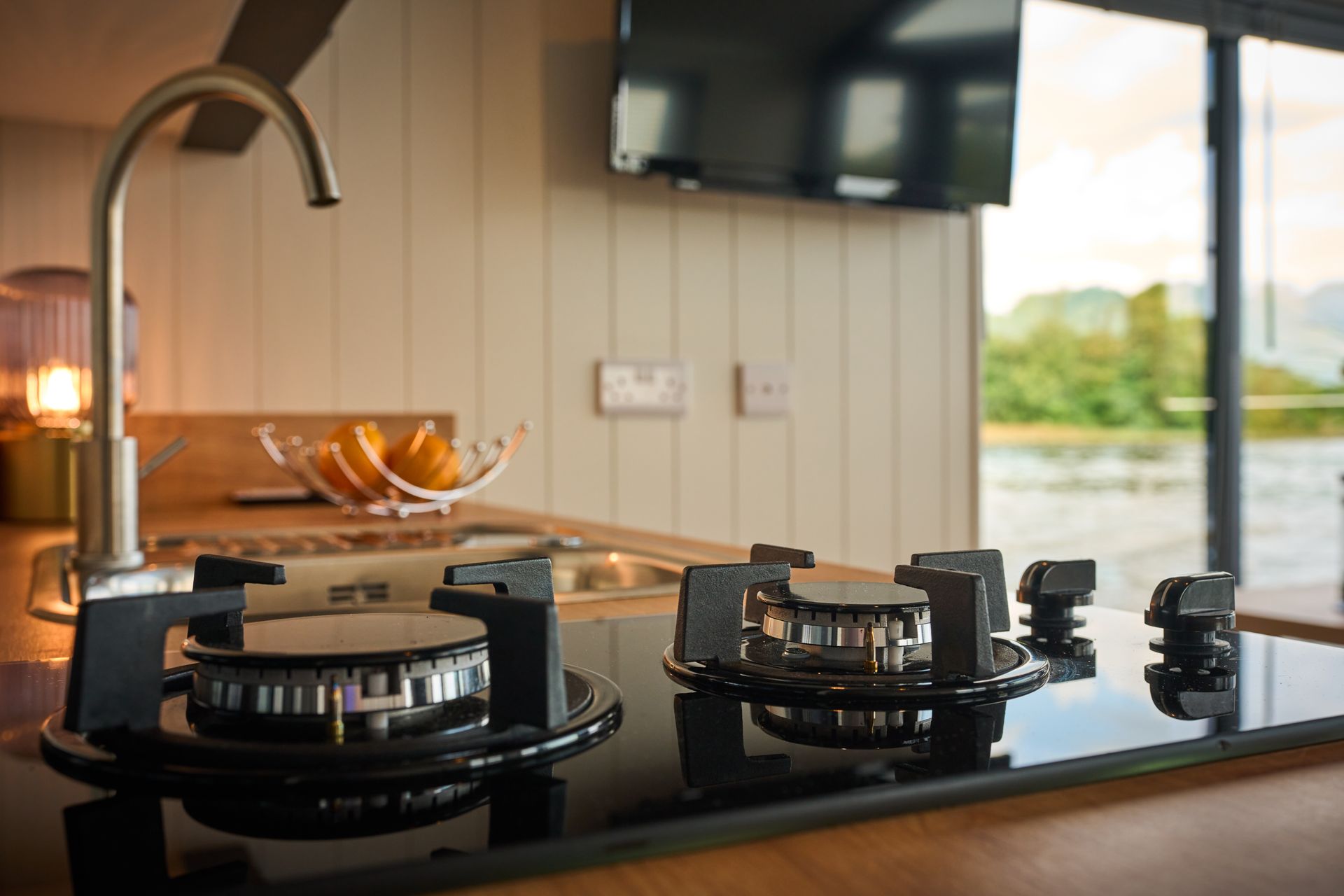A kitchen with a stove top oven , sink , and television.