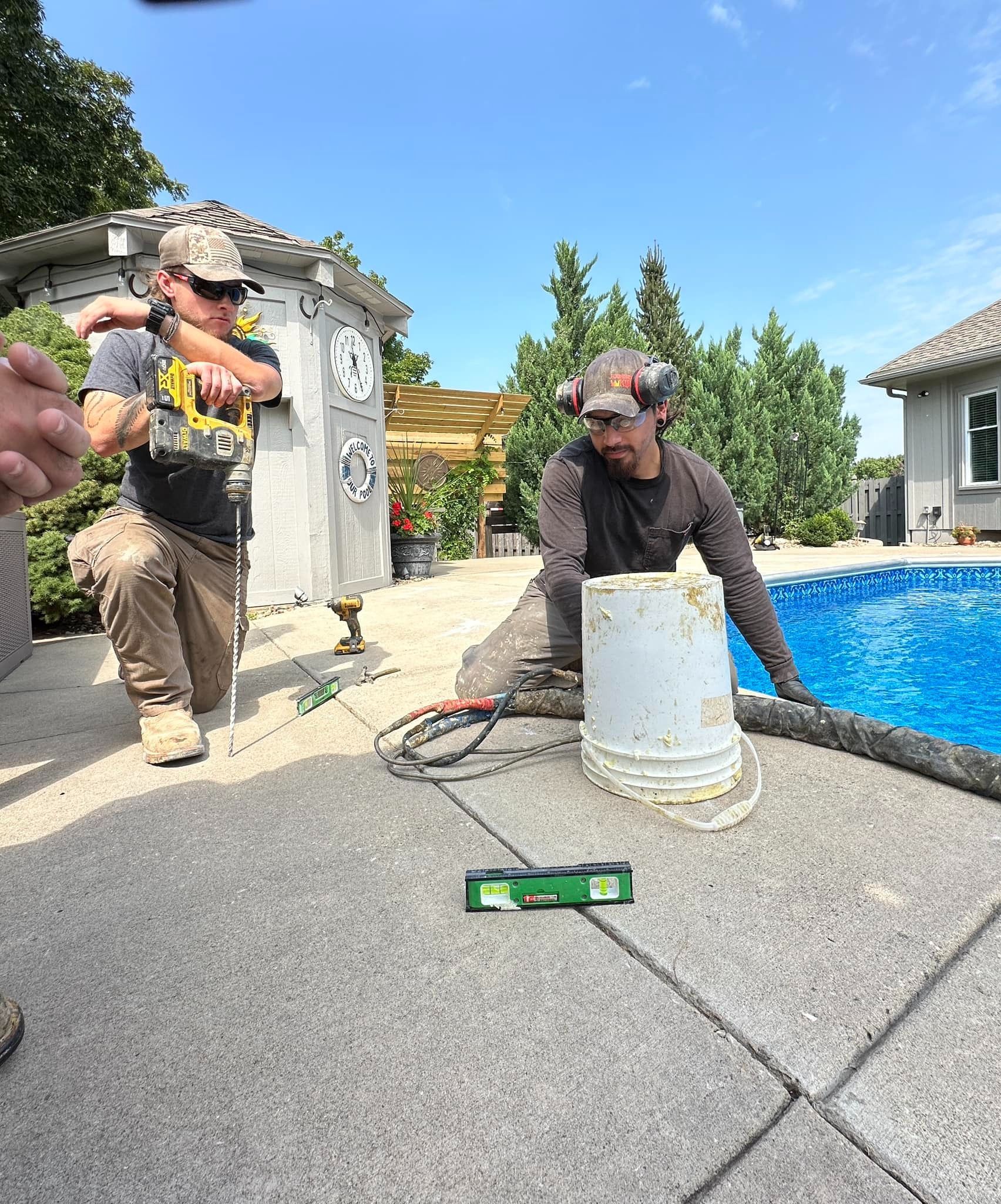 Two men are working on a patio next to a swimming pool.