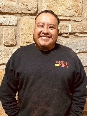 A man wearing a black sweatshirt is smiling in front of a stone wall.