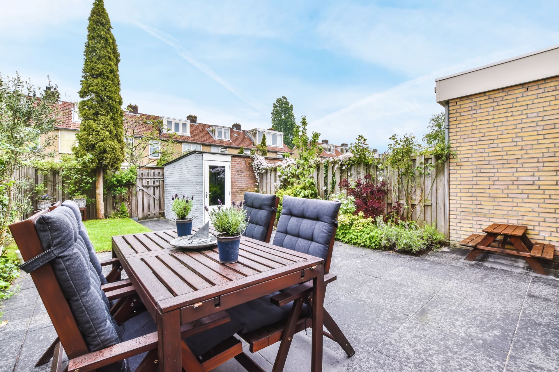Patio with wooden table and chairs, potted plants, gravel ground, and a garden wall in the background