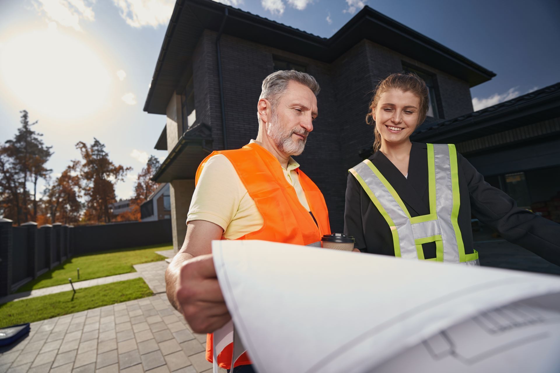 Man and woman in safety vests review blueprints in front of a house.