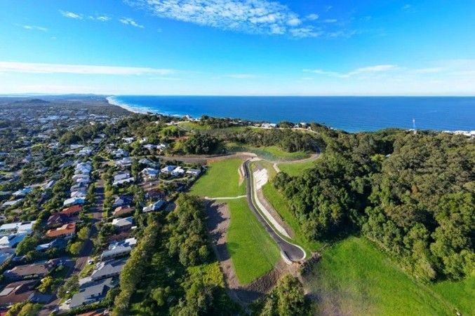 Aerial view of a coastal neighborhood beside a green hillside and blue ocean under a clear sky