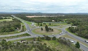 Aerial view of a roundabout on a highway surrounded by green forest and hills under a cloudy sky