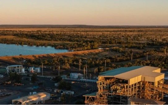 Aerial view of a riverside construction site beside a wide waterway and marshland at sunset