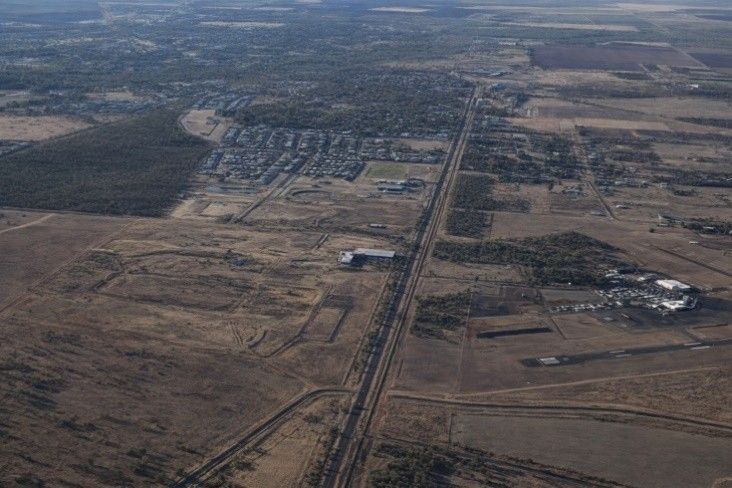 Aerial view of a rural town beside a long highway through dry, open land.