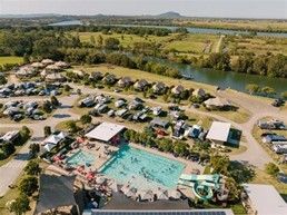 Aerial view of a busy lakeside resort with a large turquoise pool, parked cars, and green countryside nearby