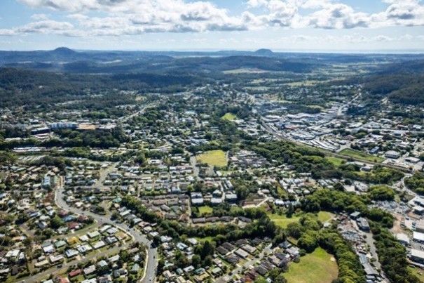 Aerial view of a sprawling suburban town with green hills and mountains under a cloudy sky