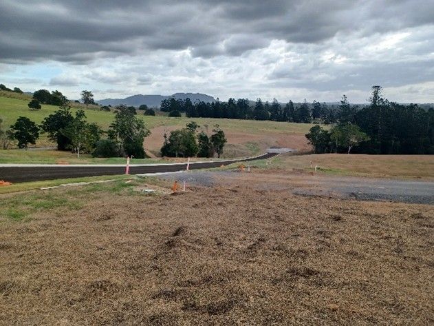 Gravel roadside beside open field and trees under cloudy sky, with orange cones marking a work area