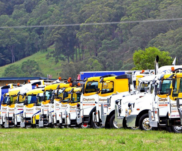 Line of white and yellow utility trucks parked on grass with a forested hill in the background