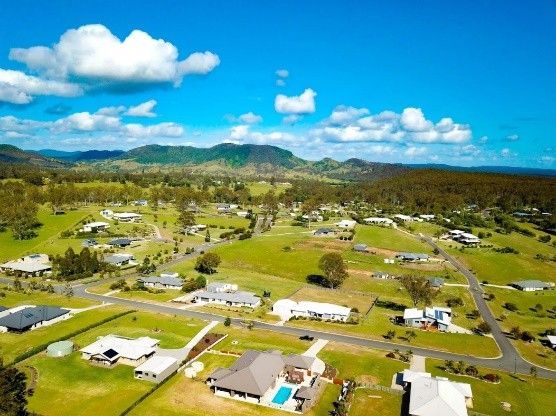 Aerial view of a green suburban neighborhood with scattered houses, roads, and mountains under a blue sky