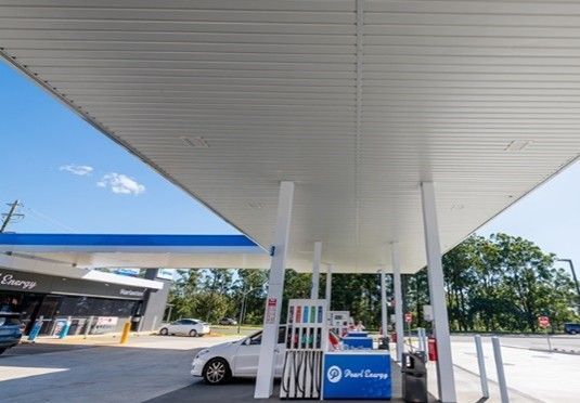 Gas station canopy with fuel pump, parked car, and blue sky on a sunny day