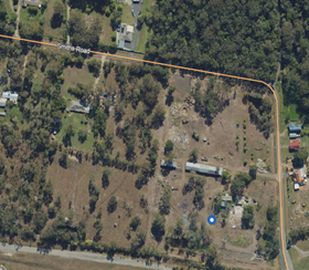 Aerial view of a rural property with scattered trees, buildings, a dirt road, and fenced grassy land
