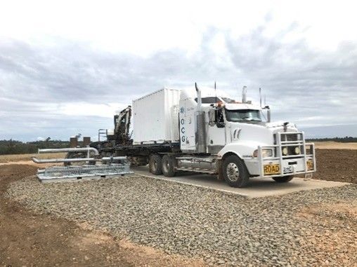 White semi-truck hauling a flatbed trailer on a gravel road under a cloudy sky
