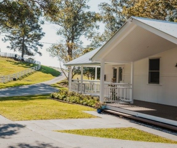 White house with porch beside a curving driveway on a sunny, grassy hillside