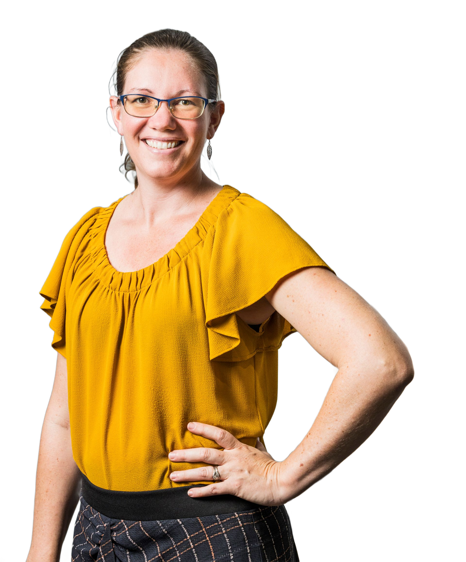 Woman with glasses smiling, wearing a yellow blouse and patterned skirt, posing with a hand on her hip.