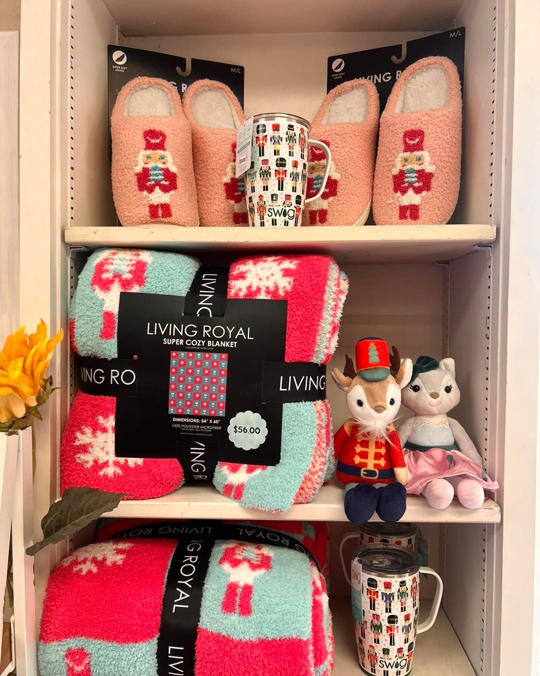 A shelf with a blanket , slippers , mugs , and a nutcracker on it.