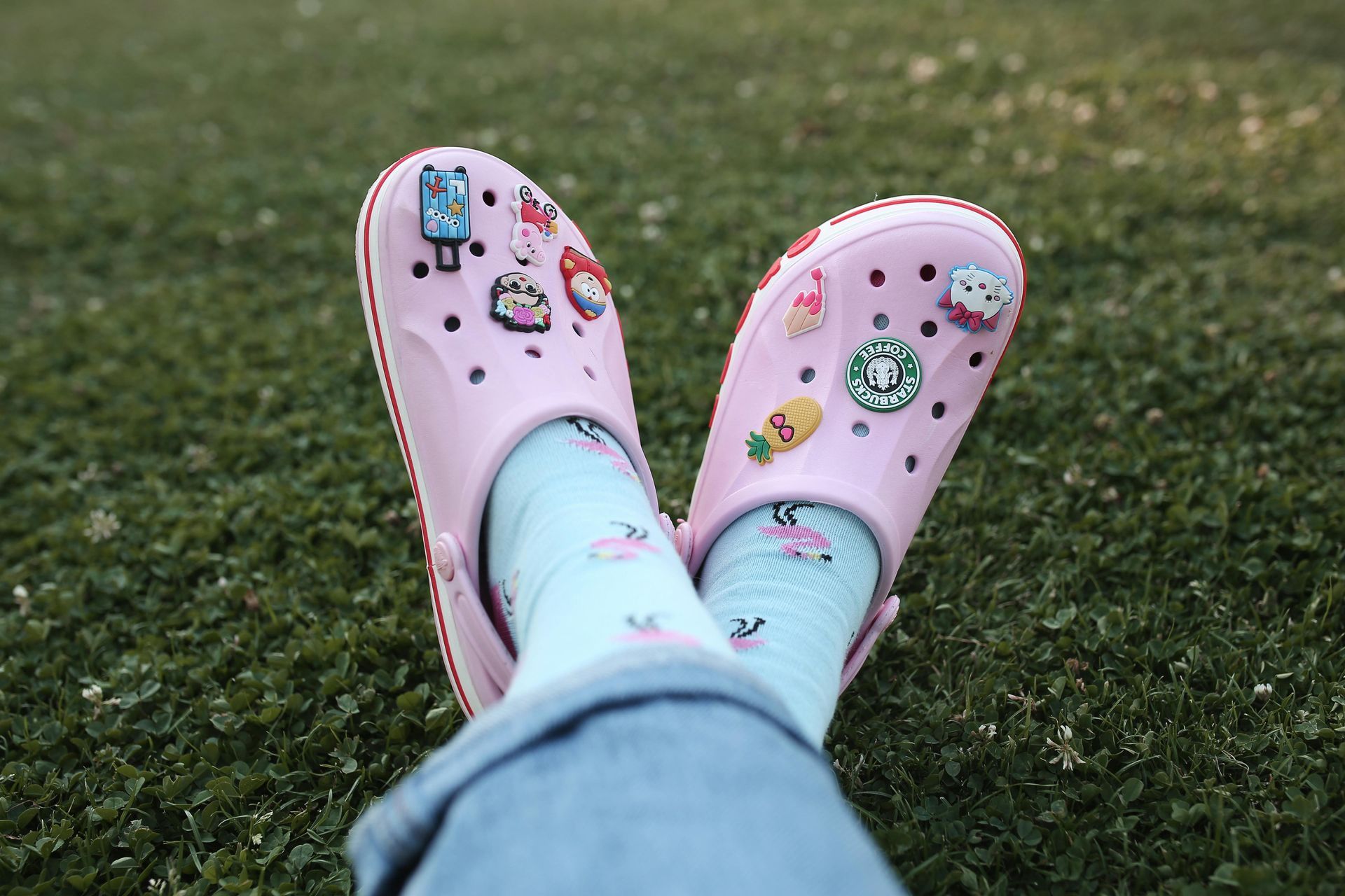 A person wearing pink crocs and blue socks is laying on the grass.