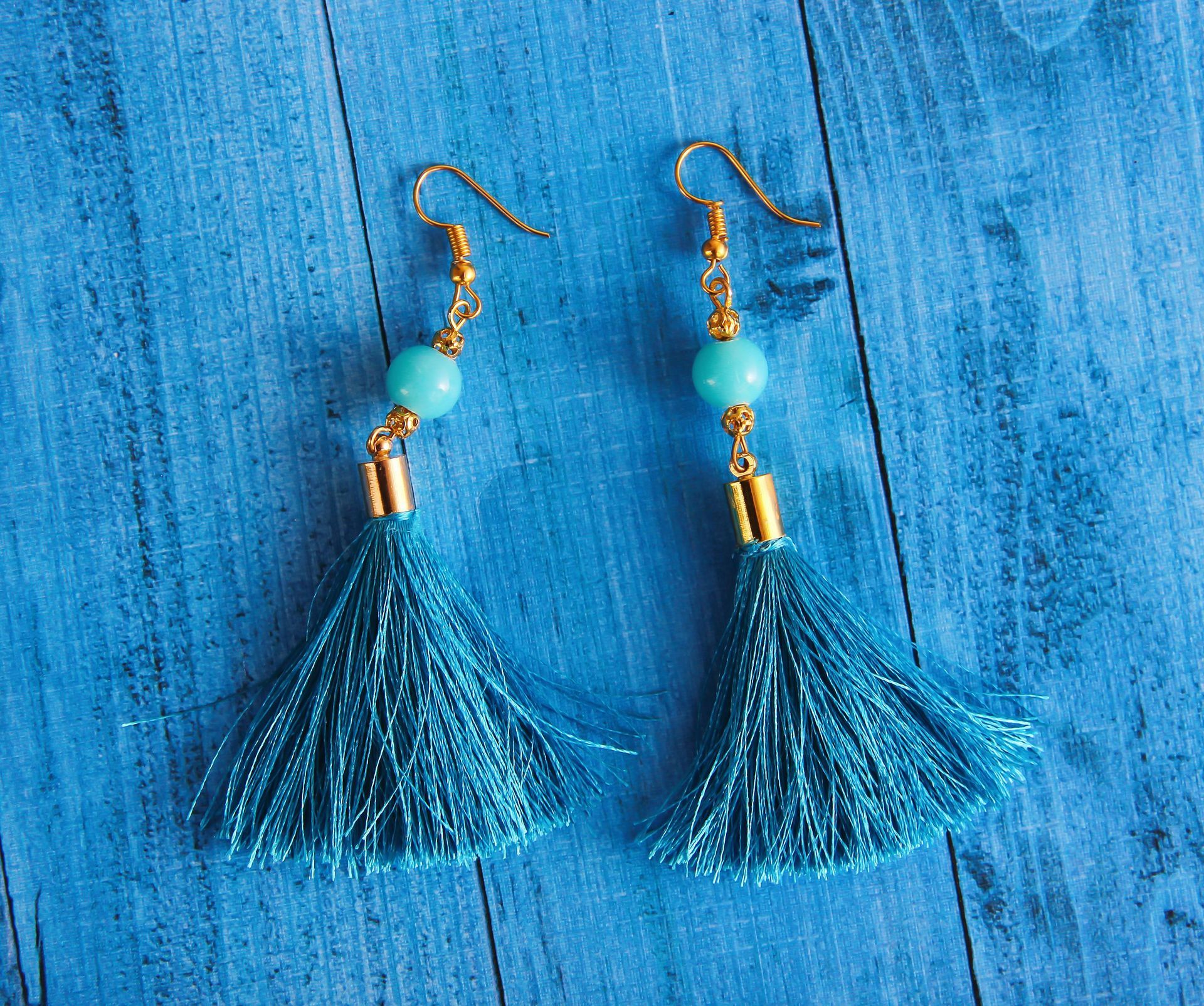 A pair of blue tassel earrings with turquoise beads on a blue wooden surface.