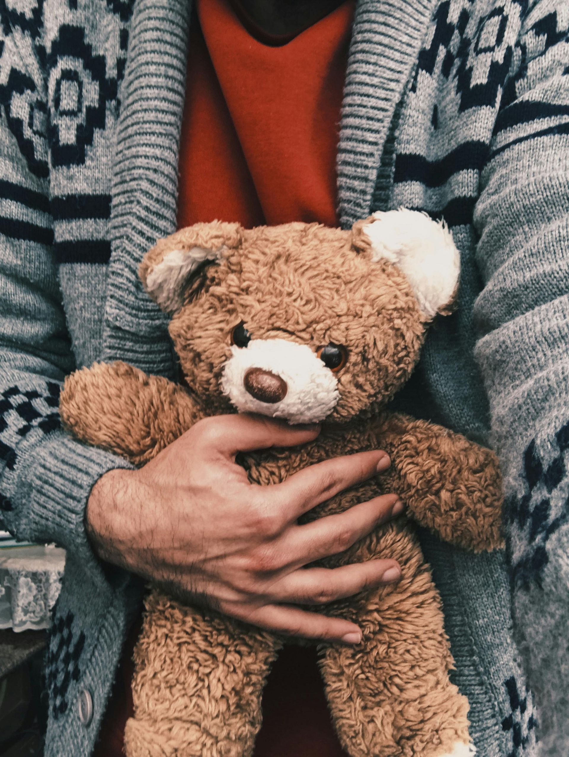 A man in a sweater is holding a teddy bear