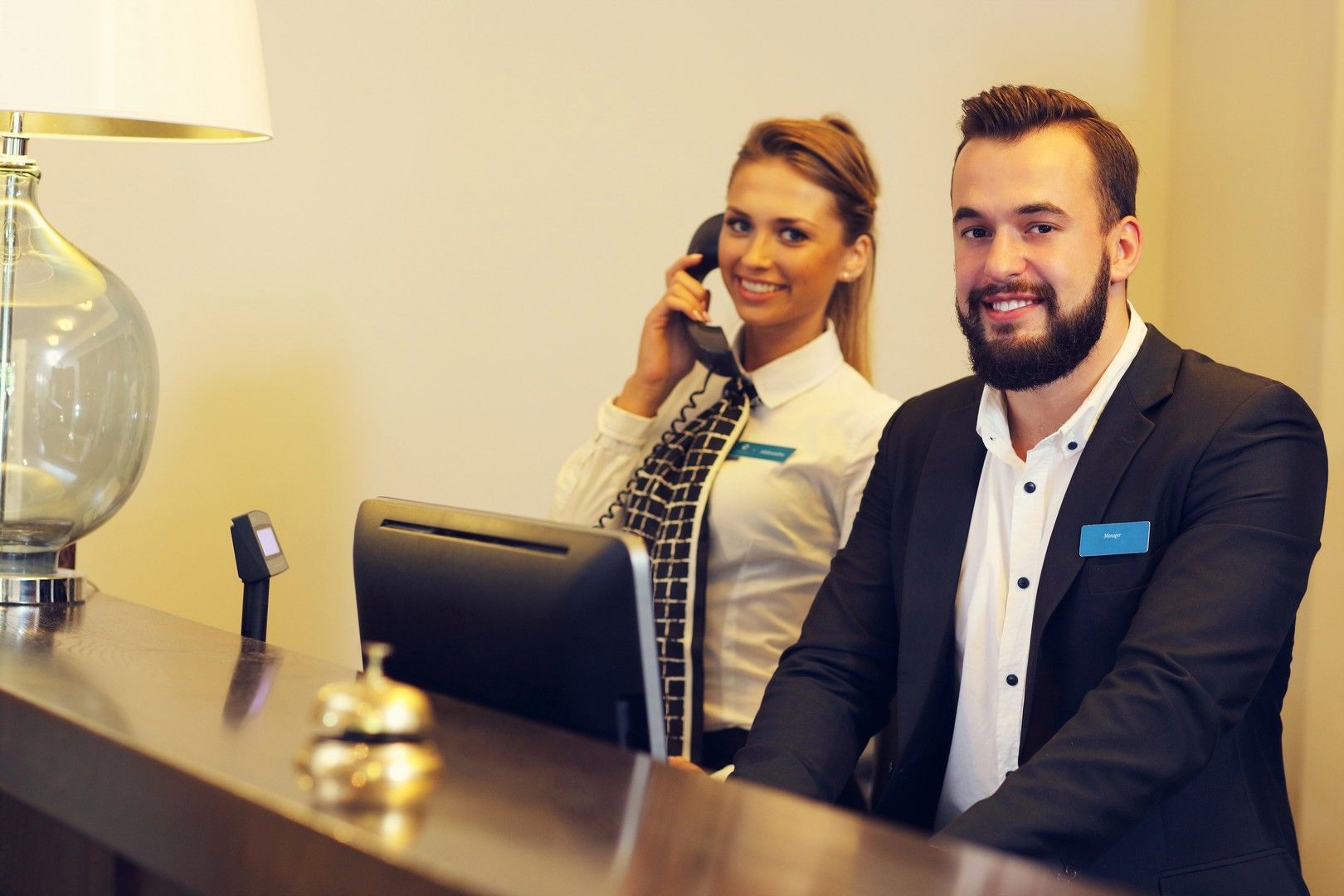 Receptionisti di un hotel dietro una scrivania, uno al telefono, l'altro sorridente.