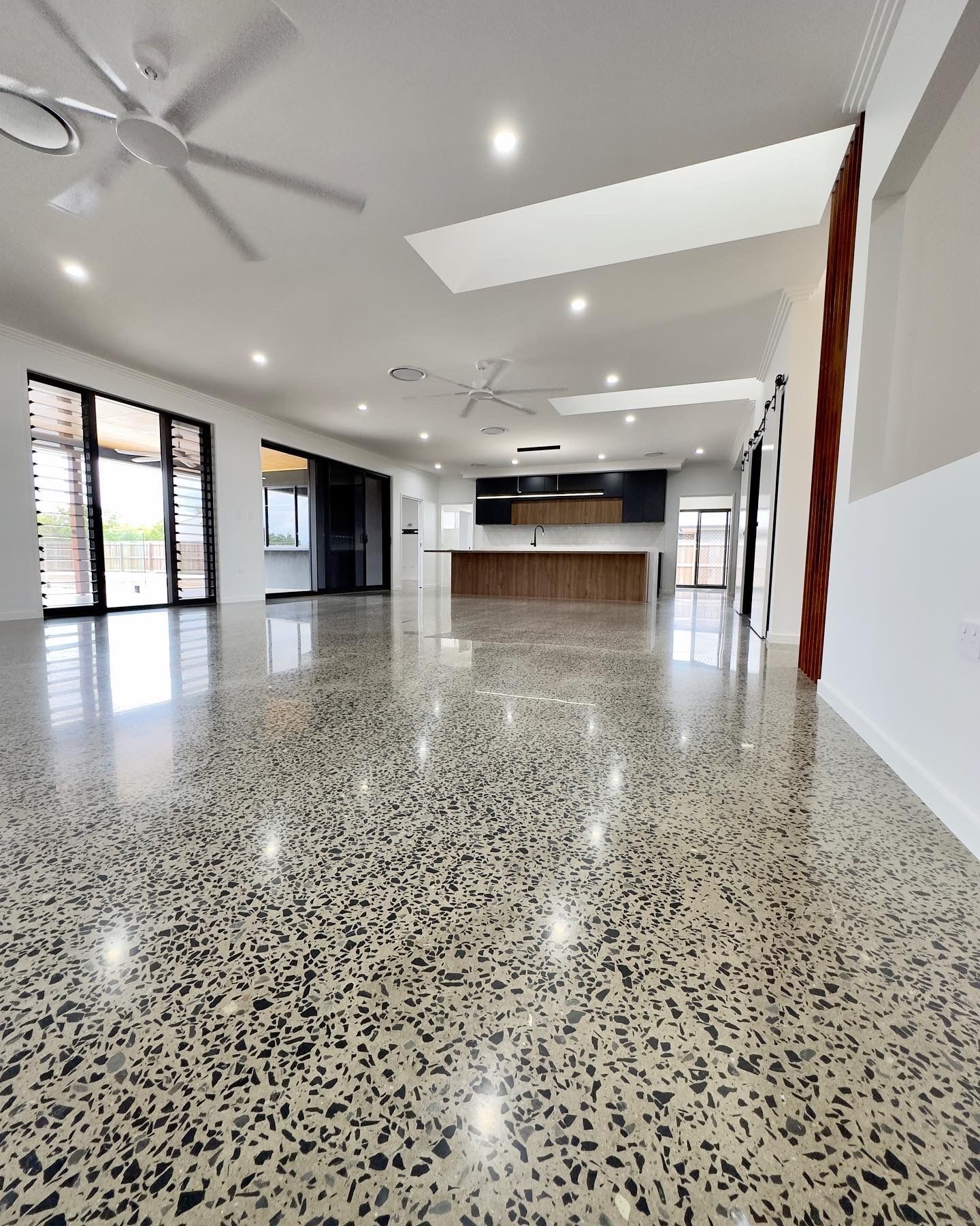 Spacious, polished concrete floor interior with kitchen in the background, windows, and ceiling fans. — Showcase Concrete & Polishing in Moore Park Beach, QLD