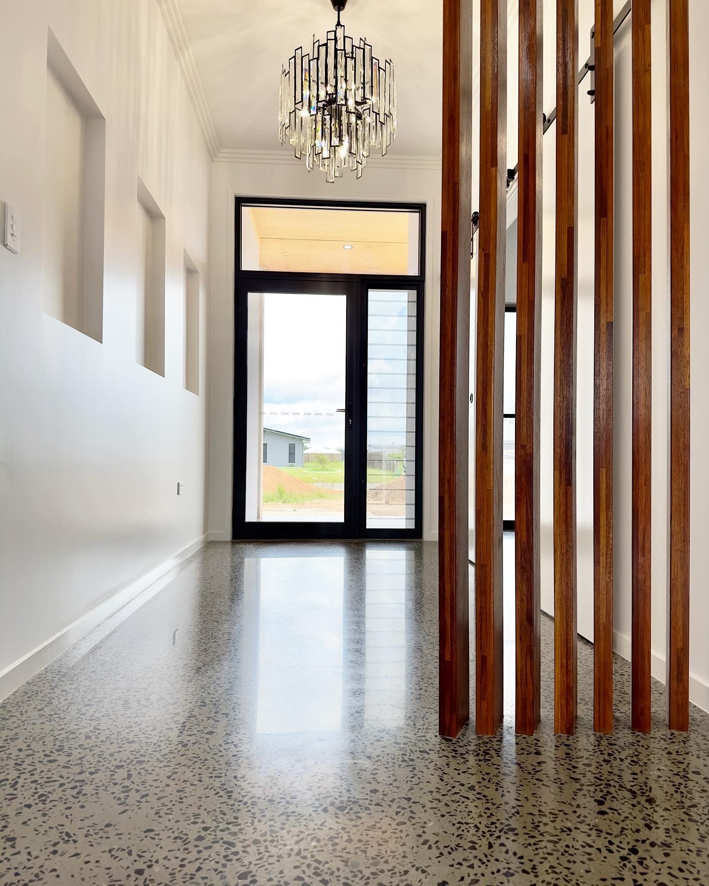 Polished concrete hallway with wooden slat divider, chandelier, and a view through double doors. — Showcase Concrete & Polishing in Moore Park Beach, QLD