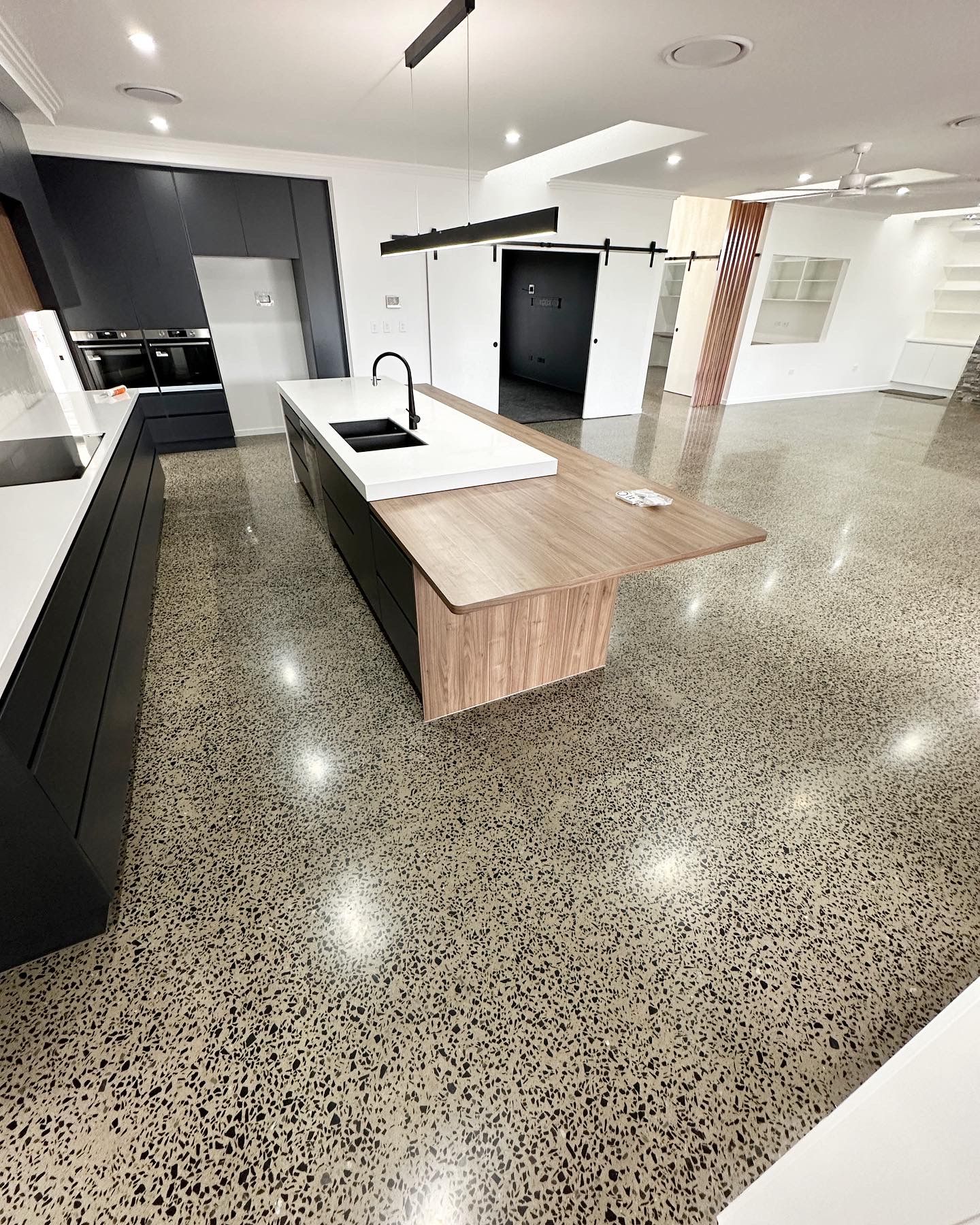 Modern kitchen showroom with island, dark cabinets, and terrazzo floor. — Showcase Concrete & Polishing in Moore Park Beach, QLD