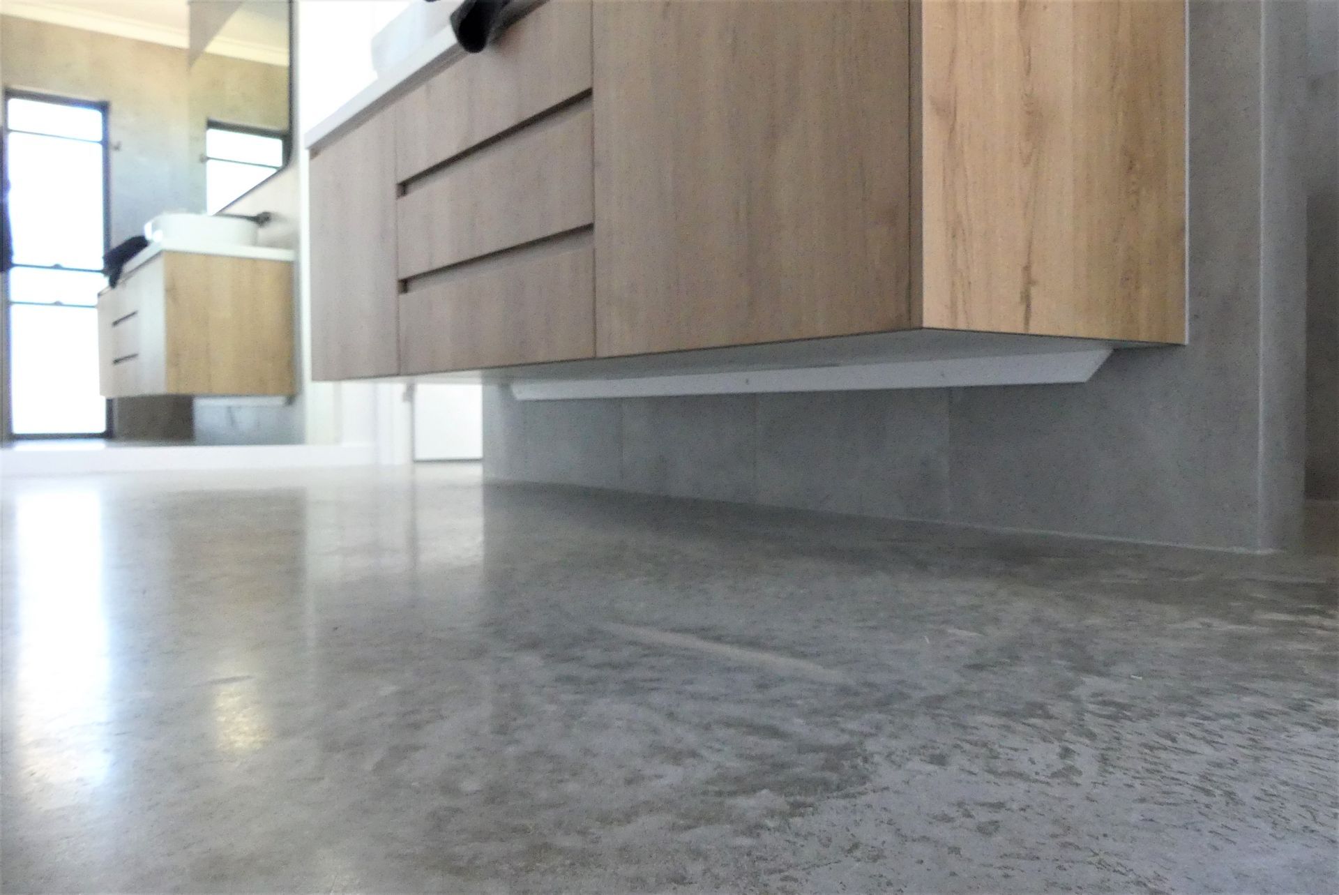 Shiny, grey concrete floor in a modern bathroom with light wood cabinets and a floating vanity. — Showcase Concrete & Polishing in Moore Park Beach, QLD