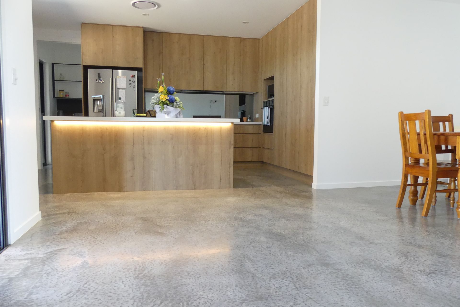 Modern kitchen with light wood cabinets, an island, and polished concrete floors. — Showcase Concrete & Polishing in Moore Park Beach, QLD