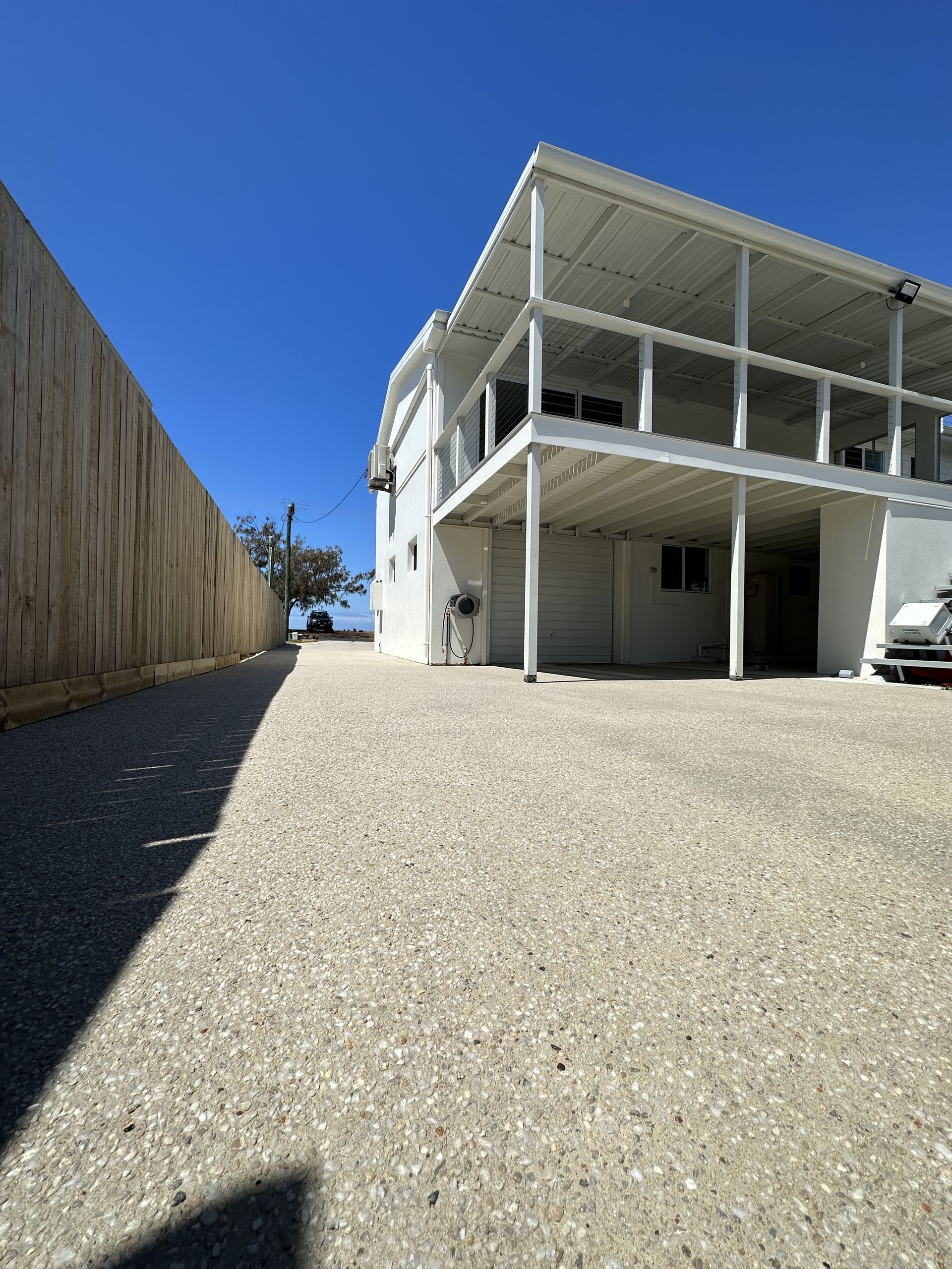 White two-story building with balcony, gravel driveway, tall wooden fence, and blue sky. — Showcase Concrete & Polishing in Moore Park Beach, QLD