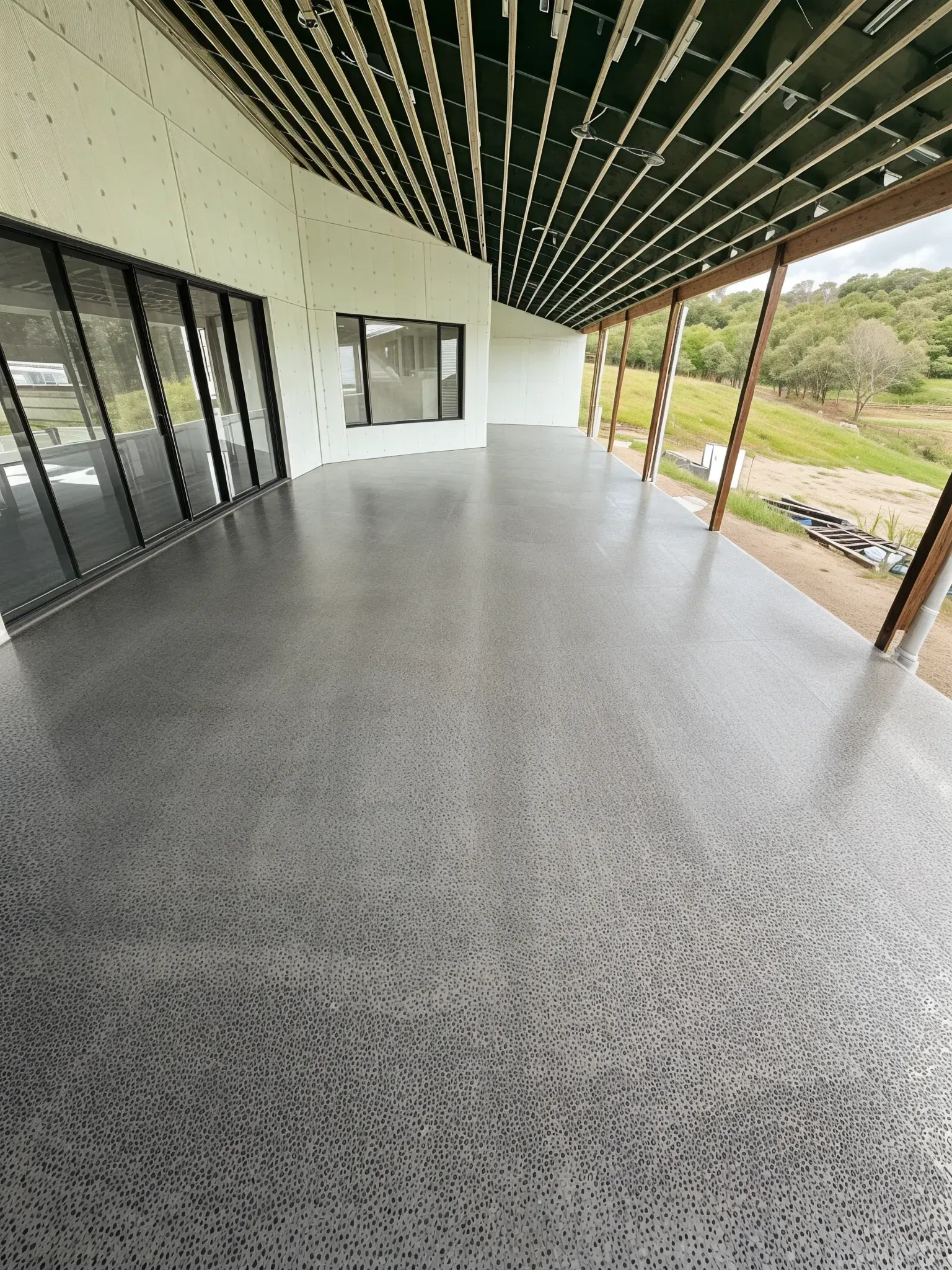 Exterior view of a covered patio with a gray concrete floor, glass doors, and a natural landscape. — Showcase Concrete & Polishing in Moore Park Beach, QLD