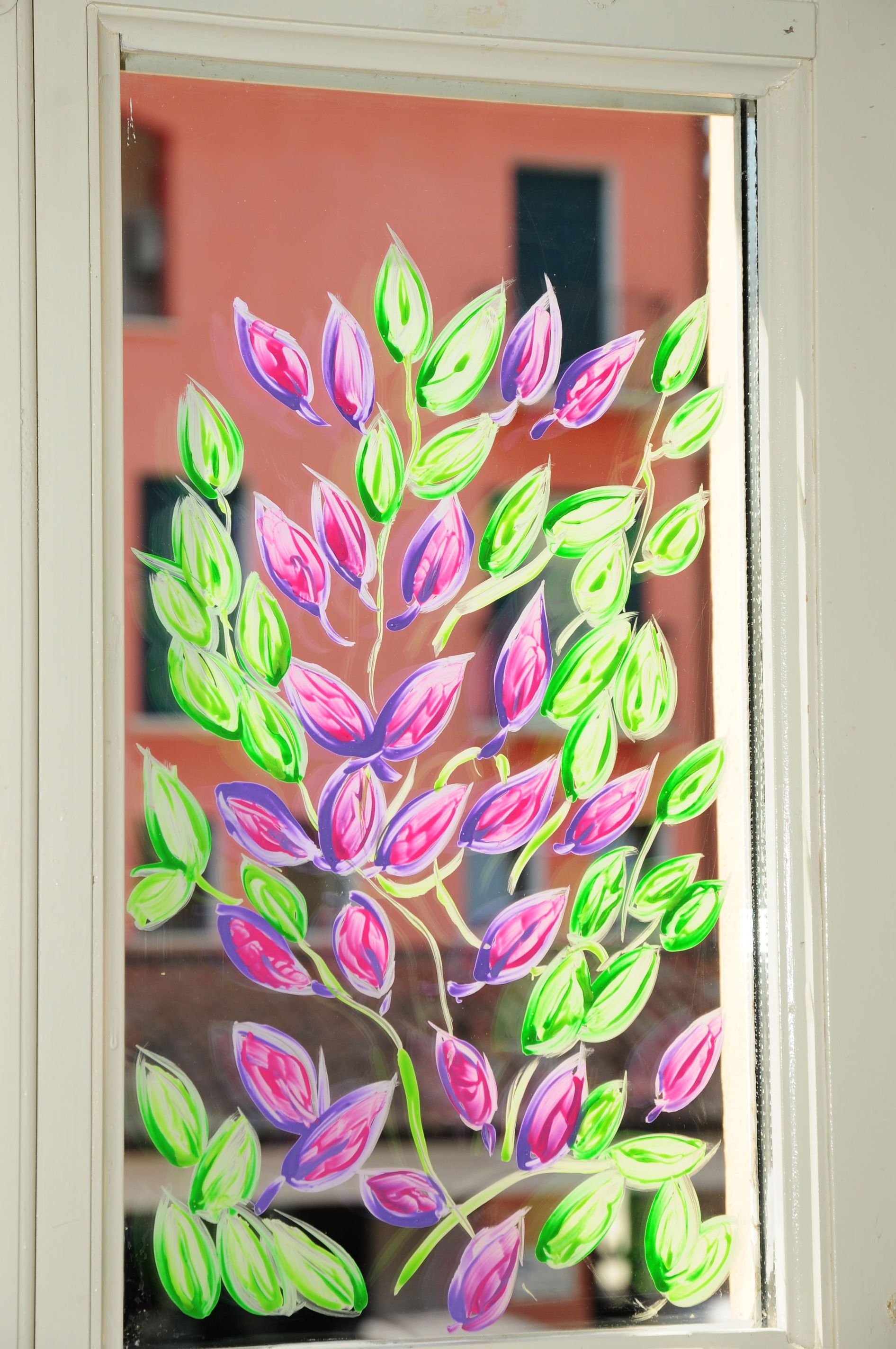 Un dipinto di un albero con fiori rosa e foglie verdi su una finestra.