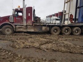 A picture of a red bed truck covered in mud and hooked onto a tank.