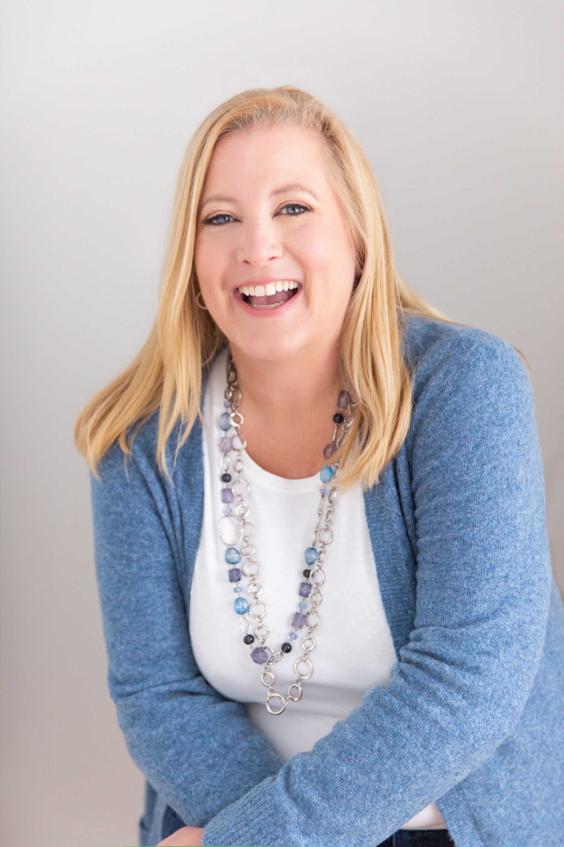 A woman wearing a blue sweater and a necklace is smiling.