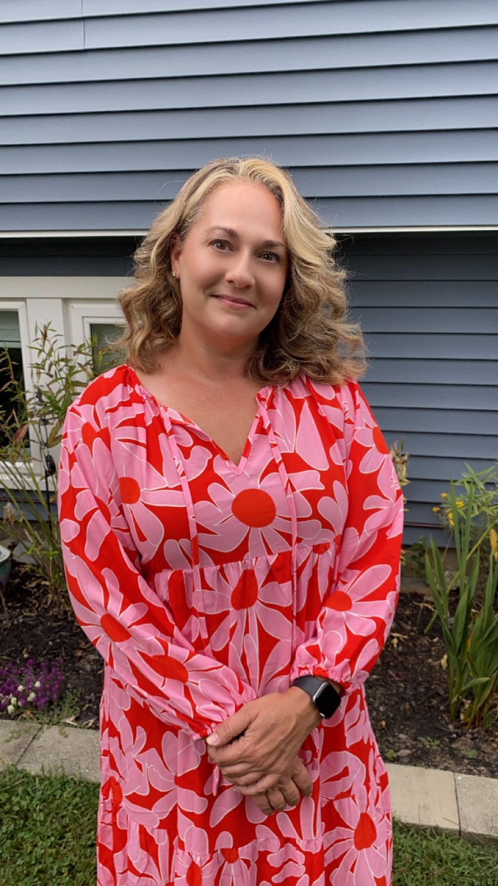 A woman in a red and pink dress is standing in front of a blue house.