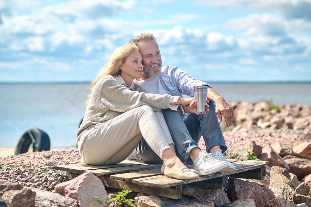 A man and a woman are sitting on a wooden dock near the ocean.