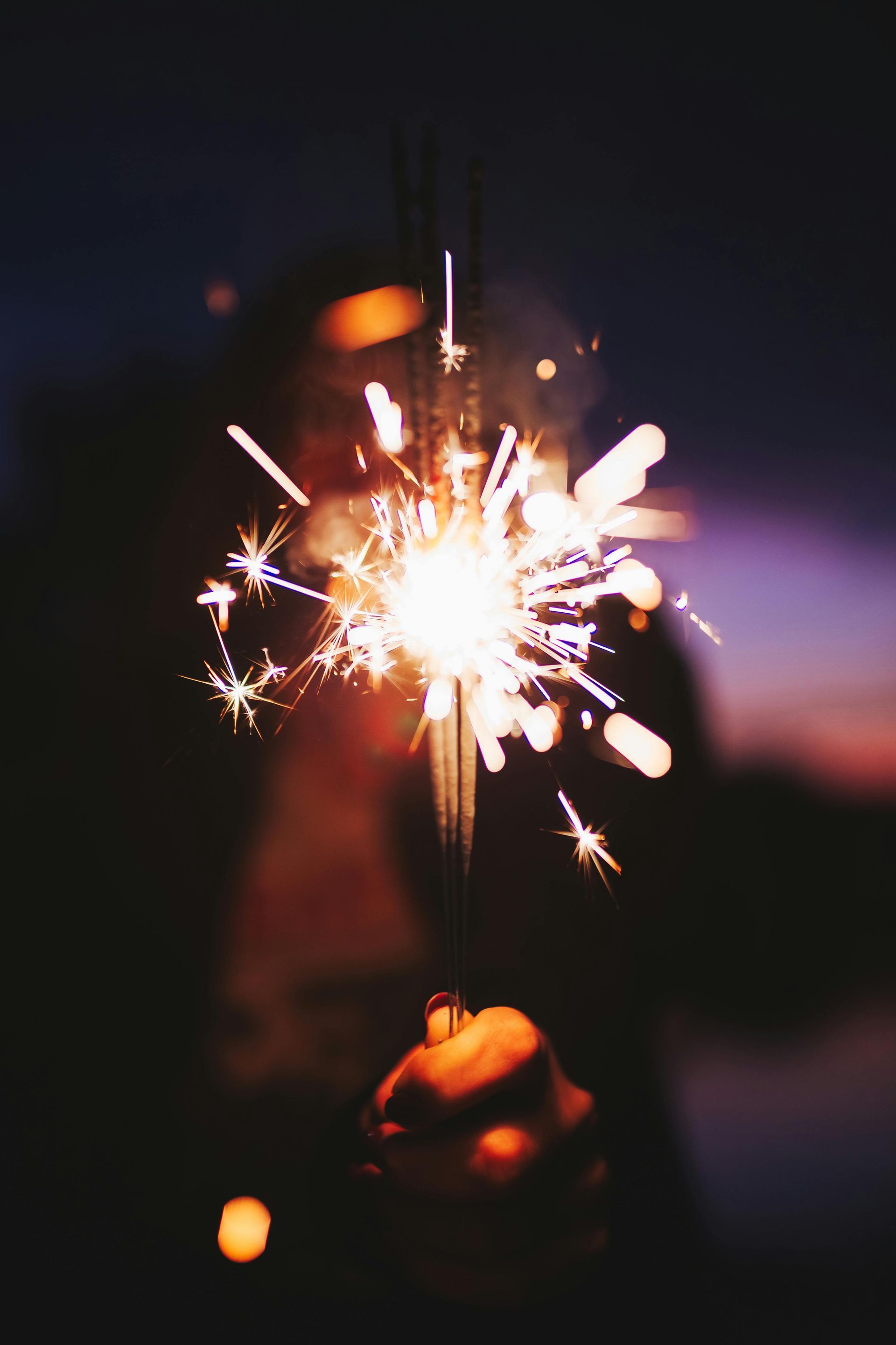 A person is holding a sparkler in their hand at night.