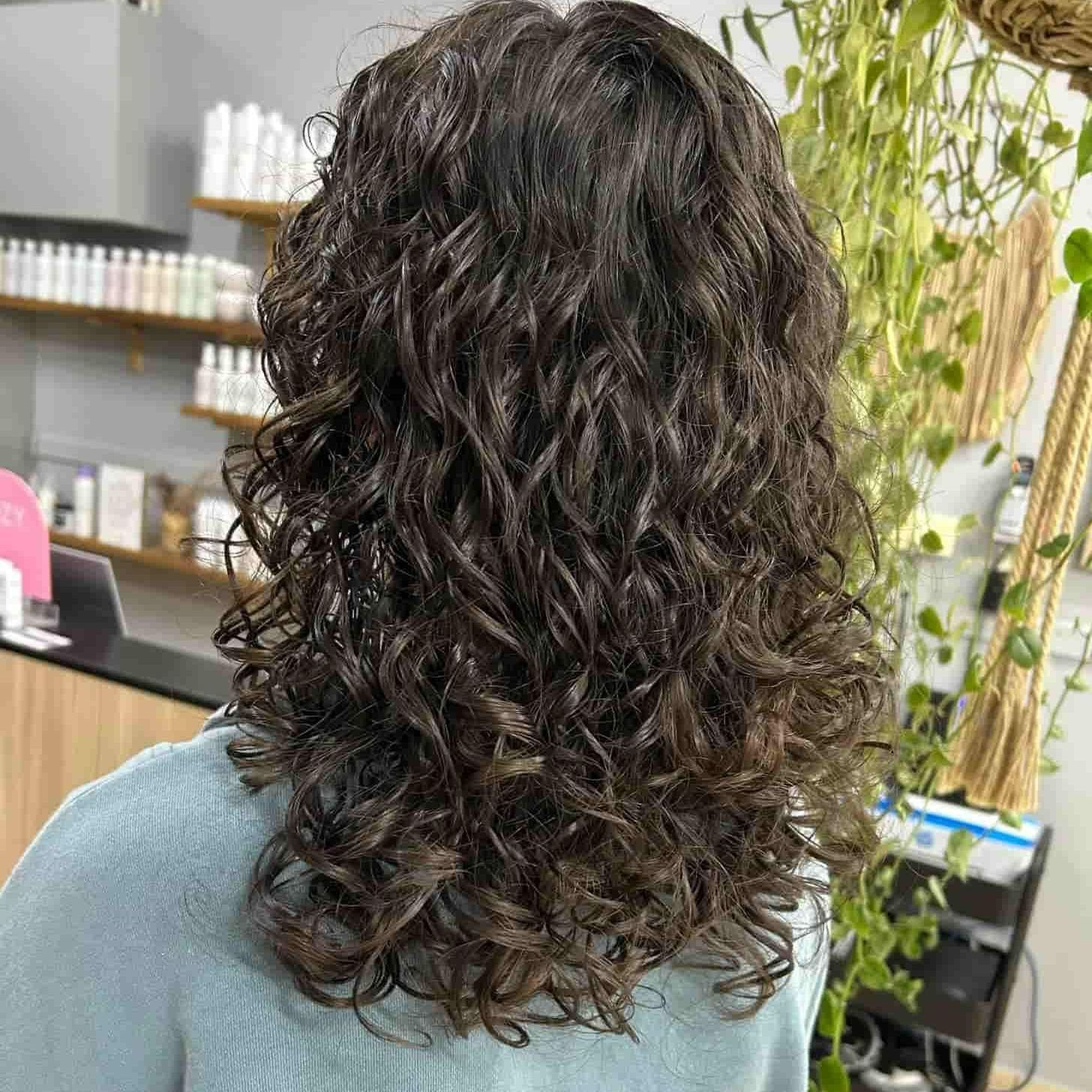 A woman with long curly hair is standing in a salon — M & Co Hair Salon In Atherton, QLD