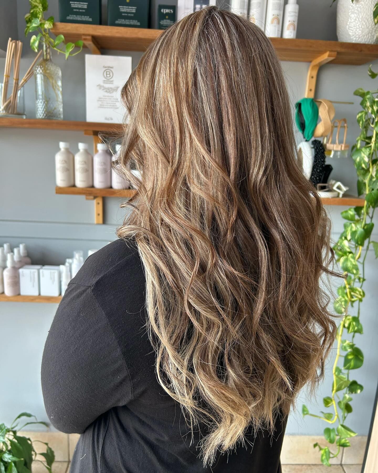 A woman with long hair is standing in front of a shelf with bottles on it — M & Co Hair Salon In Atherton, QLD