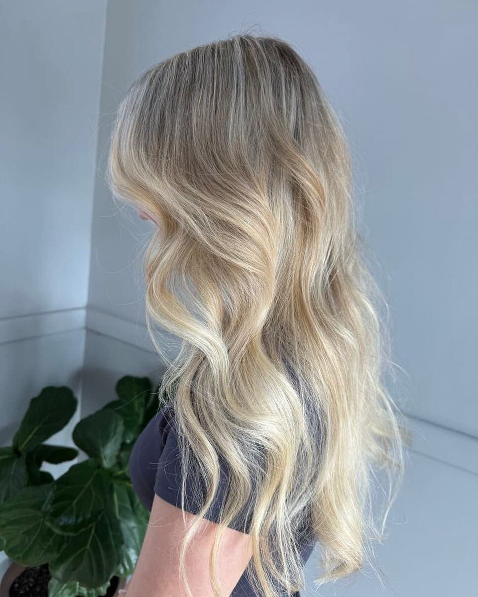 A woman with long blonde hair is standing next to a plant — M & Co Hair Salon In Atherton, QLD