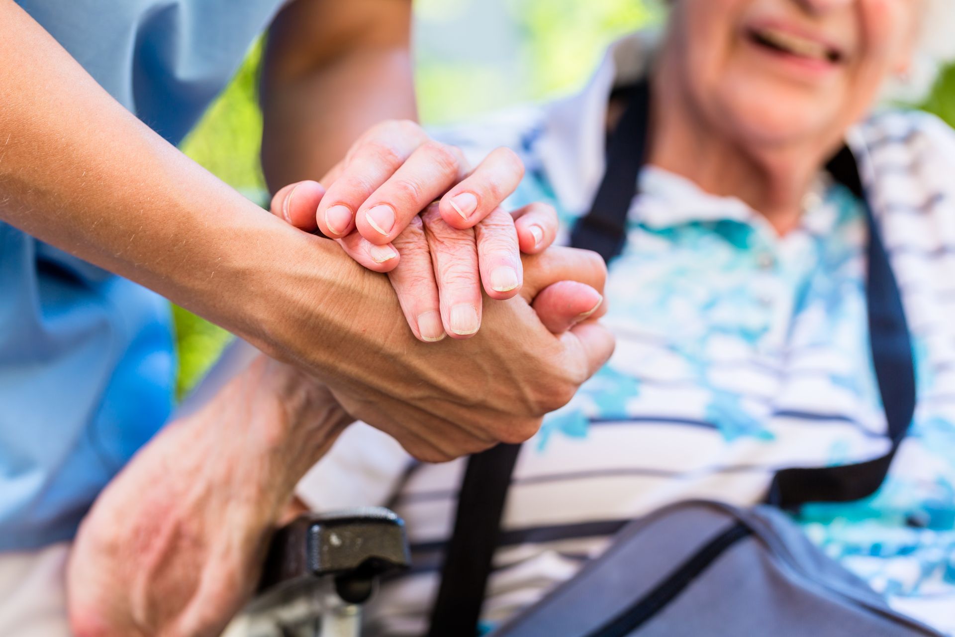 Hands clasped together in a supportive gesture beside a smiling person in a wheelchair