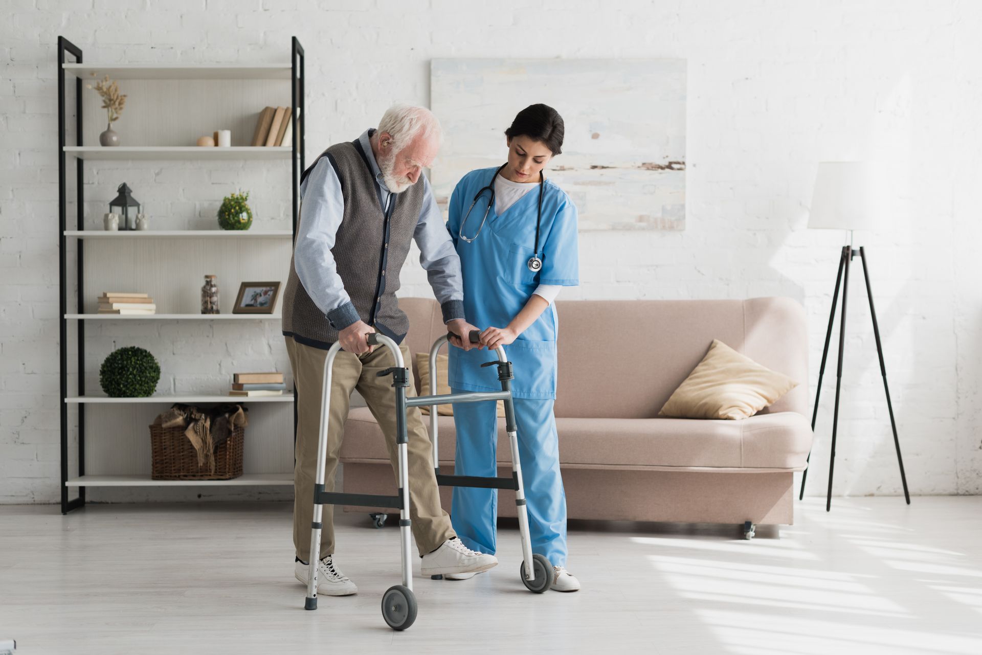 Caregiver helping an older adult walk with a walker in a bright living room