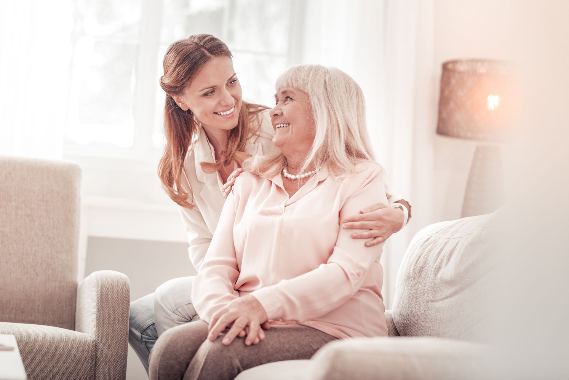 Two women smiling and embracing on a couch in a bright living room
