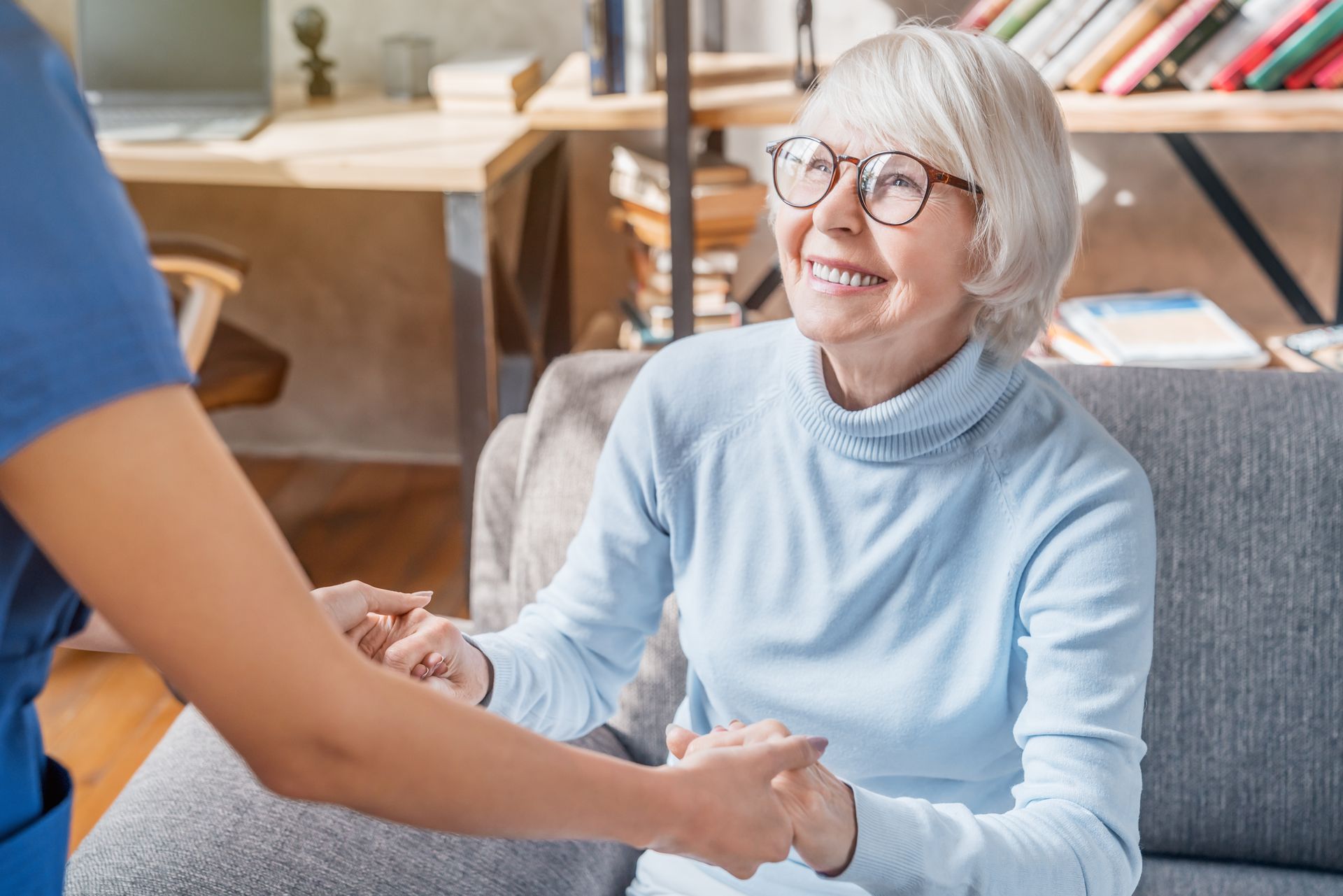 Older woman smiling and holding hands with a caregiver in a cozy living room