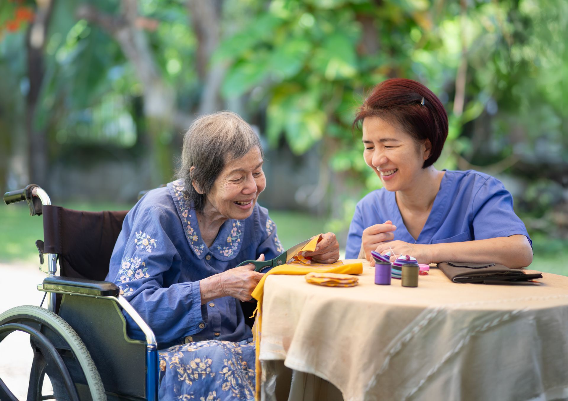 Two women smiling at a table outdoors, sharing tea and conversation near a wheelchair