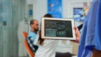 a dentist is holding a tablet with an x-ray of a patient's teeth