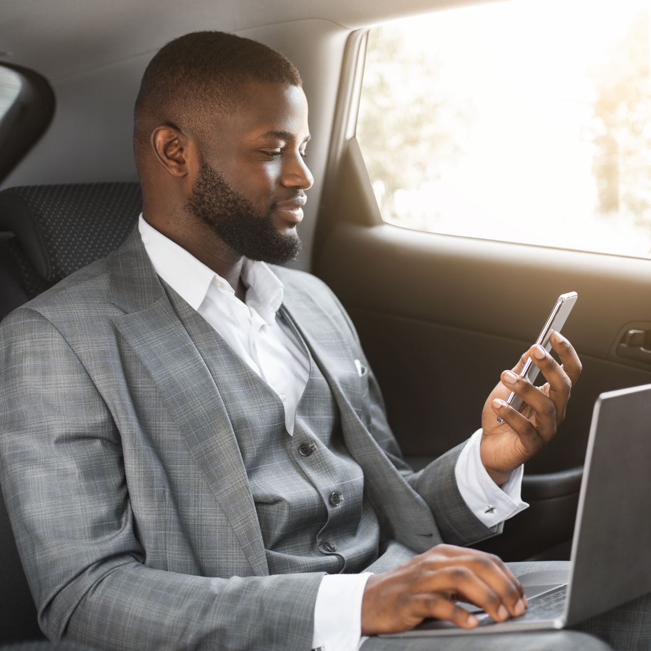 a man in a suit is using a laptop and looking at his phone